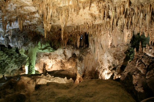 A stunning cave interior with stalactites hanging from the ceiling and illuminated rock formations below.