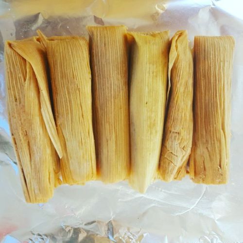 Five tamales wrapped in corn husks, arranged neatly on a silver foil surface.