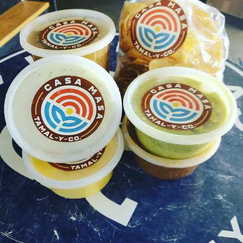 Containers of colorful sauces from Casa Masa, arranged on a surface with a logo in the background.