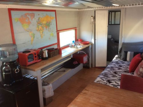 Cozy interior of a small living space featuring a map, kitchenette, and seating area with a table and water dispenser.