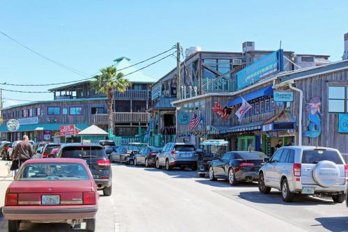 A lively street scene with shops and restaurants, featuring colorful signs and parked cars under a clear blue sky.