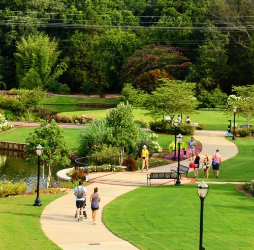 A scenic park with walking paths, greenery, flowers, and people enjoying the outdoors on a sunny day.