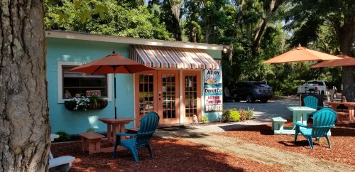 A colorful donut shop with outdoor seating, surrounded by trees and a sunny atmosphere.