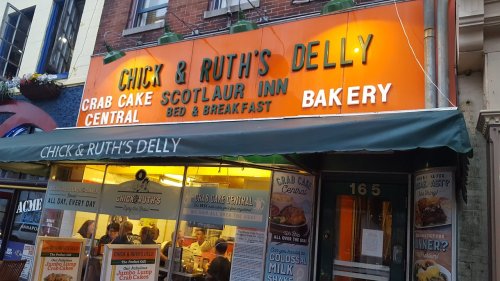 Sign for Chick & Ruth's Delly, featuring "Crab Cake Central" and "Bakery," with a green awning and bright orange lettering.