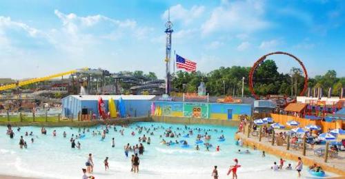 A vibrant water park scene with people enjoying a wave pool, slides, and attractions under a sunny sky.
