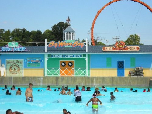 A vibrant water park scene with children swimming in a pool, colorful buildings, and a roller coaster in the background.