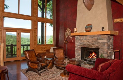 Cozy living room with a stone fireplace, wooden accents, and large windows showcasing a mountain view.