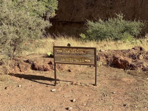 Wooden sign pointing to "Campground" and "Havasu Falls" in a desert landscape with sparse vegetation.