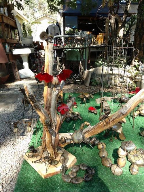 A whimsical outdoor display featuring metal insect sculptures on a wooden tree and grass-like ground.