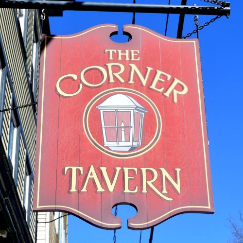 Sign for "The Corner Tavern" featuring a lantern design on a red background.