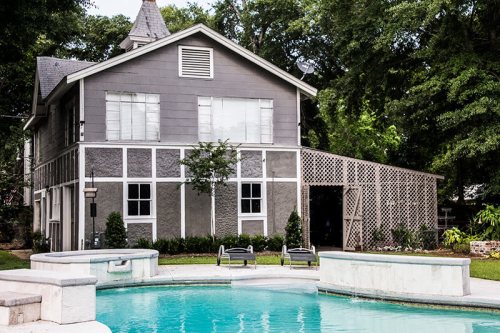 A modern two-story house with a pool and spa, surrounded by greenery and a wooden trellis structure.