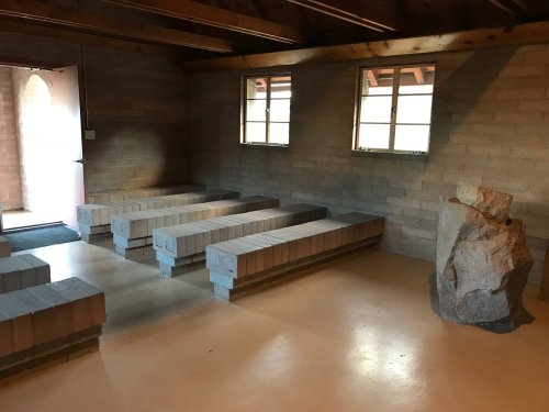 Interior of a simple room with block seating, windows, and a large rock feature in the corner.