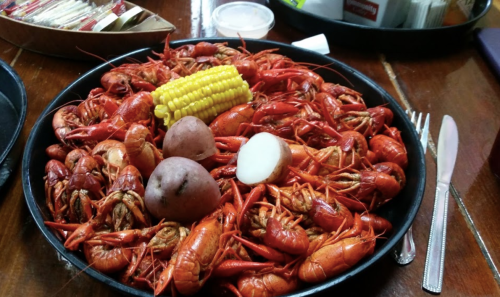 A large platter of boiled crawfish, corn on the cob, and potatoes, served on a wooden table.