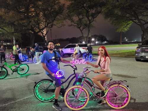 A man and woman on brightly lit bicycles at night, surrounded by others enjoying a bike event.