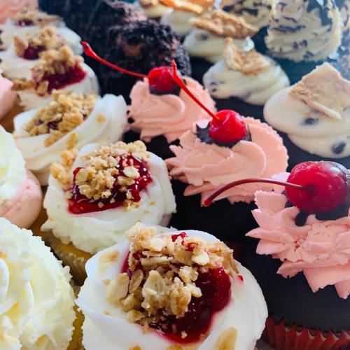A colorful assortment of cupcakes with various toppings, including cherries, nuts, and frosting.
