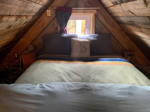 Cozy attic bedroom with a bed, decorative pillow, and a window, featuring wooden walls and a warm color palette.