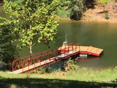 A red dock extends into a calm river, surrounded by trees and greenery.