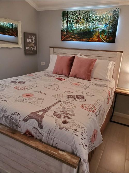 Cozy bedroom featuring a wooden bed with a patterned quilt, decorative pillows, and artwork on the wall.