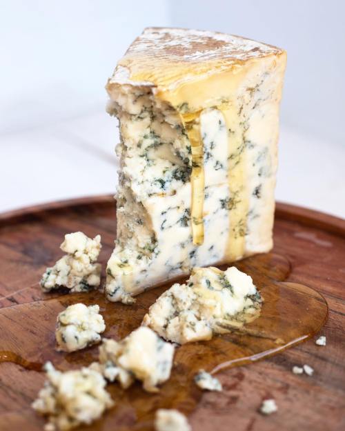 A wedge of blue cheese drizzled with honey, sitting on a wooden board with crumbled pieces around it.