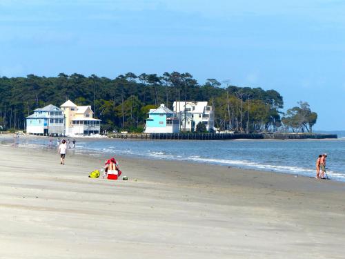 A sandy beach with colorful houses in the background, people walking, and a lifeguard station nearby.