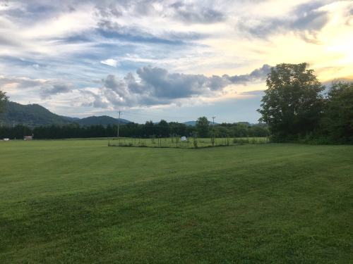 A grassy field with a fenced area and trees, set against a backdrop of mountains and a colorful sky at sunset.