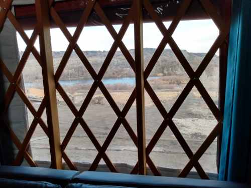 View through a lattice window of a yurt, showcasing a serene landscape with a lake and distant hills.