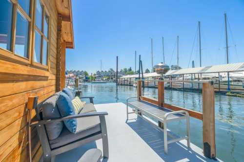 A cozy deck with seating overlooks a calm marina filled with boats and sailboats under a clear blue sky.