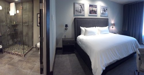 A modern hotel room featuring a king-sized bed and a glass-enclosed shower in a stylish bathroom.