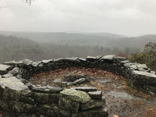 A stone circular overlook with a view of a misty forested landscape under a cloudy sky.
