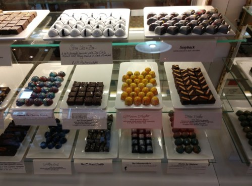 A display case filled with various colorful chocolates and truffles, neatly arranged on white plates.