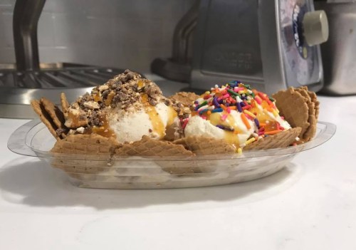 A dessert bowl with two scoops of ice cream topped with caramel, chocolate, sprinkles, and crushed cookies in a waffle bowl.
