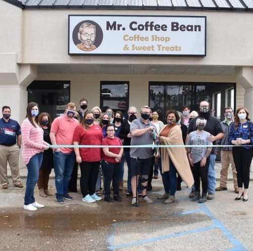 A group of people gathers outside Mr. Coffee Bean for a ribbon-cutting ceremony, all wearing masks and smiling.