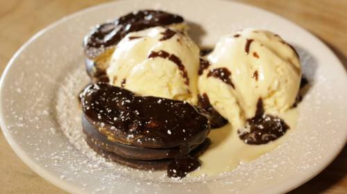 A plate with two chocolate-covered cookies and two scoops of vanilla ice cream drizzled with chocolate sauce.