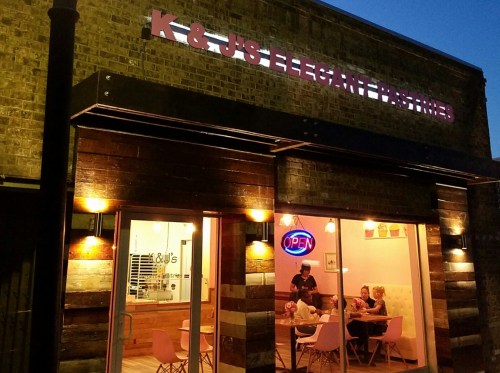 Exterior of K & J's Elegant Pastries at night, featuring an "Open" sign and patrons dining inside.