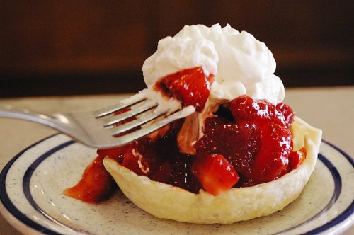 A fork lifting a bite of strawberry shortcake topped with whipped cream in a pastry shell.