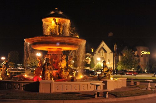 A beautifully lit fountain at night, featuring ornate sculptures, with a building in the background.