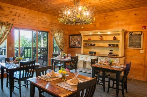 Cozy wooden dining room with tables set for a meal, a chandelier, and a sideboard displaying decorative items.