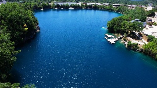Aerial view of a serene blue lake surrounded by lush greenery and a small dock on the shore.