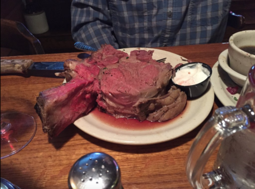 A large, juicy prime rib served on a plate with a side of dipping sauce, set on a wooden table.