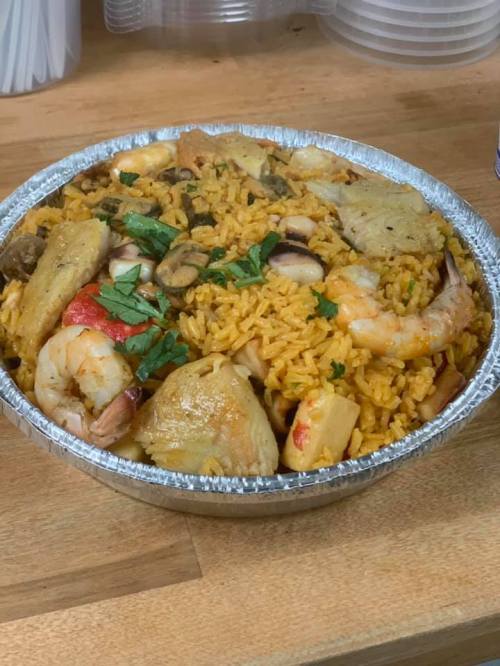 A silver foil container filled with colorful seafood rice, garnished with herbs and various pieces of seafood.