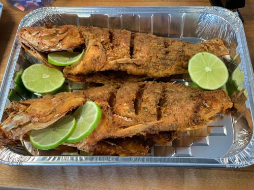 Two fried fish garnished with lime slices, served in a silver tray.