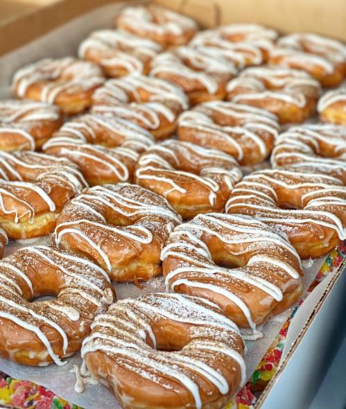 A tray of freshly glazed donuts drizzled with white icing, arranged neatly in rows.