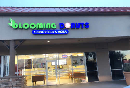 Exterior of Blooming Donuts shop, featuring a sign for smoothies and boba, with an open sign in the window.
