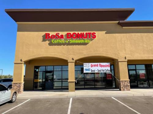 Exterior of BoSa Donuts with a grand opening banner, featuring coffee and smoothies, under a clear blue sky.