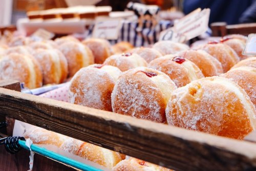 A close-up of a wooden display filled with sugar-coated donuts, some with jam filling, at a market.