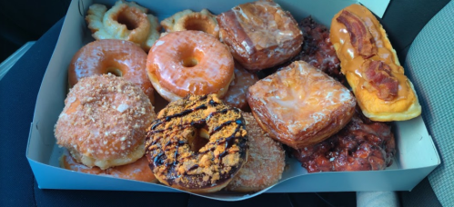 A box of assorted donuts, including glazed, chocolate, and filled varieties, with a mix of toppings and textures.