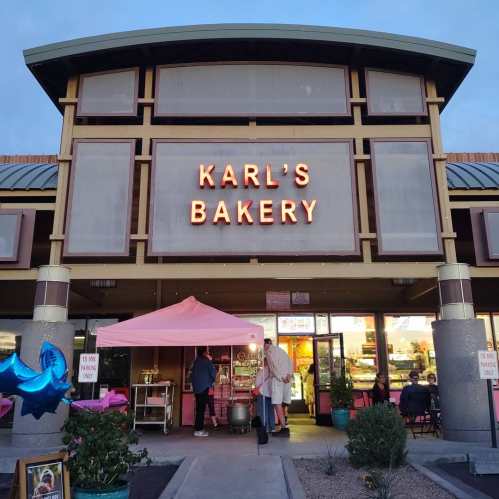 A bakery storefront with a pink tent outside, featuring a sign that reads "Karl's Bakery" in bright letters.