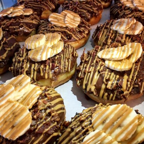 A close-up of chocolate-covered donuts topped with banana slices, drizzled with caramel and sprinkled with nuts.