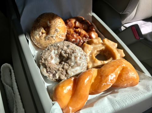 A variety of six donuts in a box, including glazed, cinnamon, and a twisted donut, on a car seat.