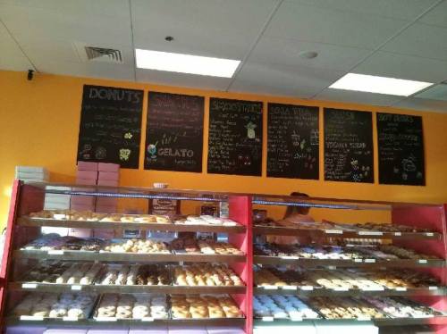 A colorful bakery display with various donuts and snacks, featuring a chalkboard menu on the wall above.